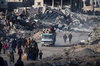 Internally displaced Palestinians walk along a street among the rubble of destroyed buildings a